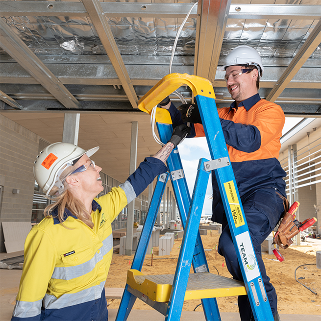 Male and female electrician wearing hard hats and working on a blue ladder